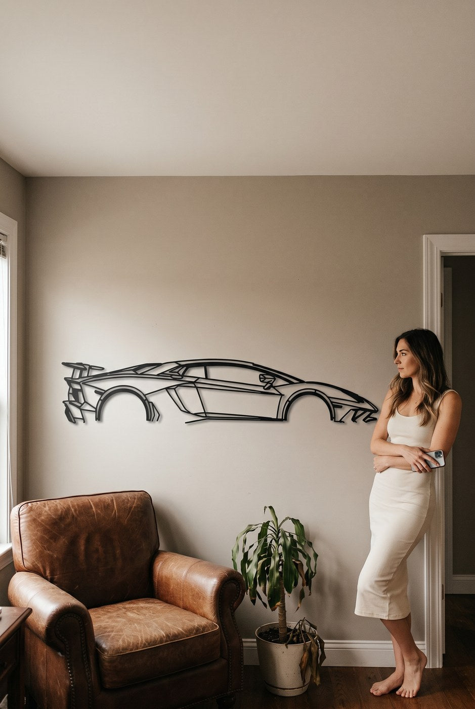 A woman hanging a matte black laser-cut steel car silhouette on a wall at home
