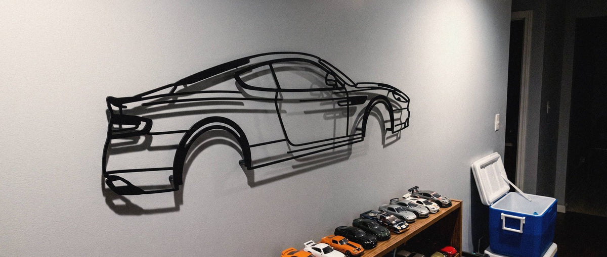 A matte black steel Aston Martin DB9 GT silhouette hanging on the wall in a hallway