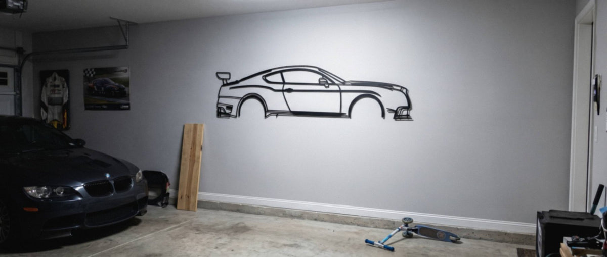 A matte black steel Bentley Continental GT3-R silhouette hanging on the wall in a finished garage